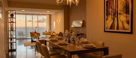 Un comedor con una larga mesa dispuesta para seis personas, una araña y un cuadro grande en la pared.