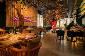 A restaurant interior with wooden tables and chairs, a neon sign on the wall, and a chef preparing food at the counter. - Apartamento 14J en YOO, Vista al mar con 2 recámaras (Panamá)