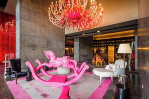 A lobby with a large chandelier, a pink horse sculpture, and a red wall. - Apartamento 14J en YOO, Vista al mar con 2 recámaras (Panamá)