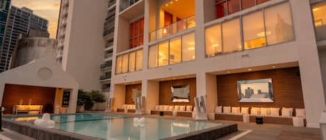 Un hotel moderno con piscina en la azotea, varios balcones y vistas del horizonte urbano.