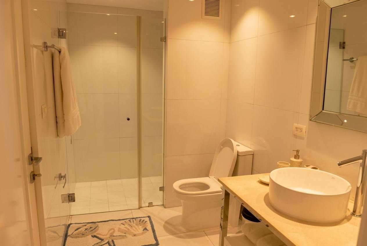 A modern bathroom with a glass shower enclosure, a toilet, and a sink with a mirror above.