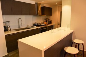 A modern kitchen with dark cabinets, a white countertop, a built-in stove, a microwave, and a blender. - Apartamento 14J en YOO, Vista al mar con 2 recámaras (Panamá)