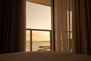 A room with a large window, curtains, and a view of a body of water and distant land. - Apartamento 14J en YOO, Vista al mar con 2 recámaras (Panamá)