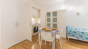 A compact kitchen with white cabinets, a dining table set for four, and a sofa with a patterned cover. - AP4 - Apartment in the heart of Milan (Milano)