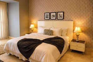 A hotel room with a large bed, two bedside tables with lamps, a headboard with framed pictures, and a patterned wall. - 20B Apartamento de 1 recamara, con vista al mar (Panamá)