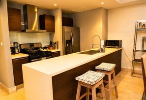A modern kitchen with a central island, stainless steel appliances, and wooden stools. - 20B Apartamento de 1 recamara, con vista al mar (Panamá)