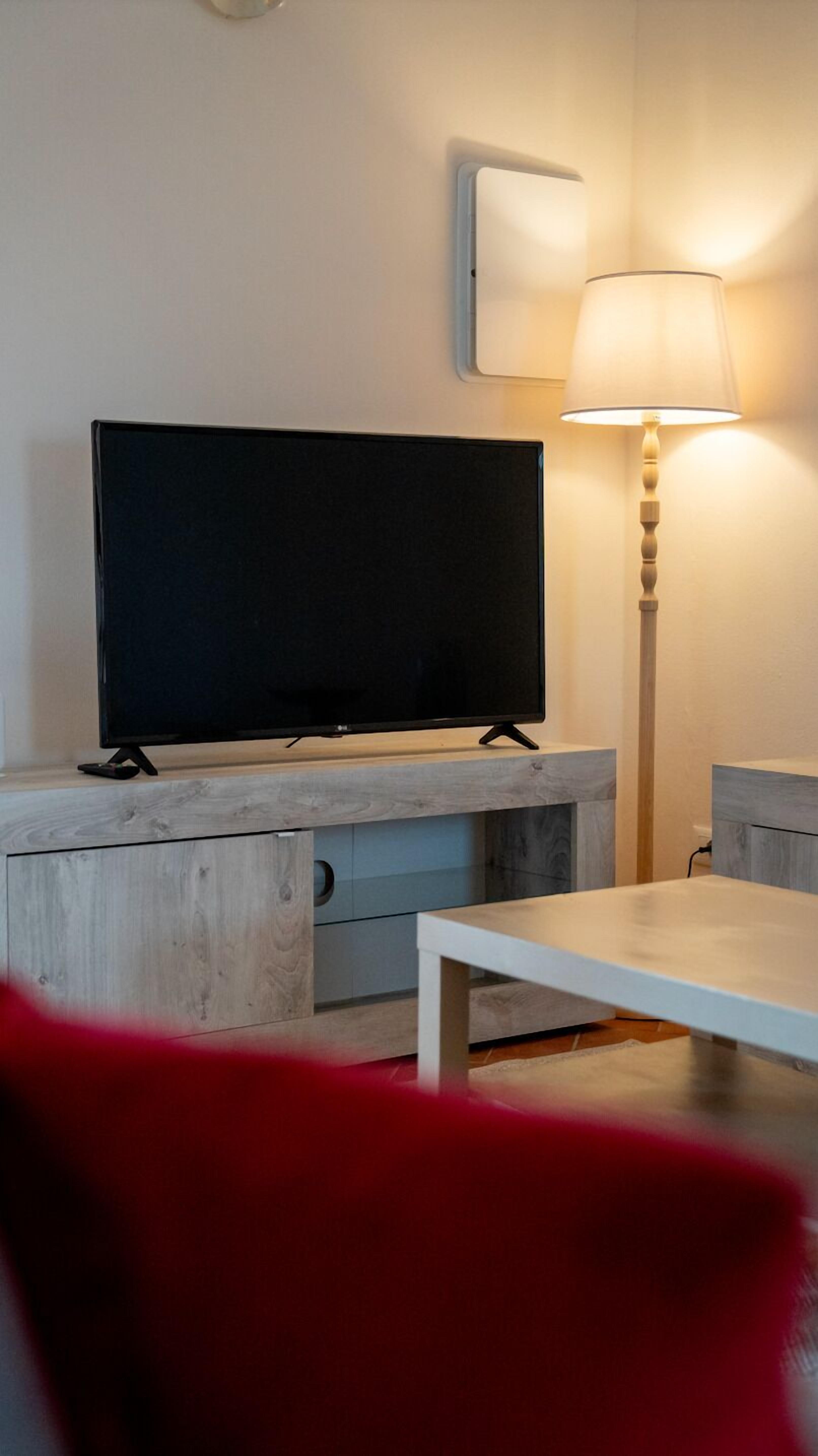 A living room with a flat-screen TV, a lamp, a table, and a red chair.