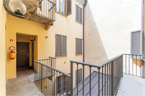 A narrow stairway with metal railings leading to a door, a fire extinguisher on the wall, and a building with a beige facade and shutters. - AP6 Apartment in the Cathedral area (Milano)