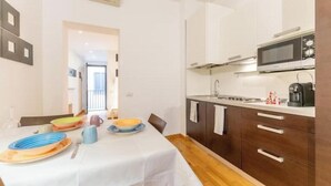 Une cuisine compacte équipée d’un four à micro-ondes, d’une cuisinière et d’une machine à café. On y trouve une table à manger avec des assiettes et une chaise.