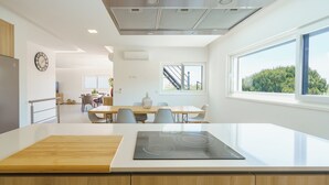 Una cocina moderna con una isla central, un comedor con sillas, una escalera y vistas a zonas verdes.