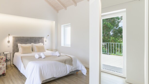 Een slaapkamer met een groot bed, een klein nachtkastje, een raam en een balkon.