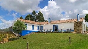 Een gebouw met twee verdiepingen, een pannendak, een stenen gevel en een buitenkant in blauw en wit. Er zijn zitgedeeltes buiten met parasols.