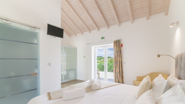 A hotel room with a bed, a television, a sliding glass door, and a balcony with a view. - Room 'Monte Do Sol 3' with Mountain View, Wi-Fi and Air Conditioning (S. Luís)