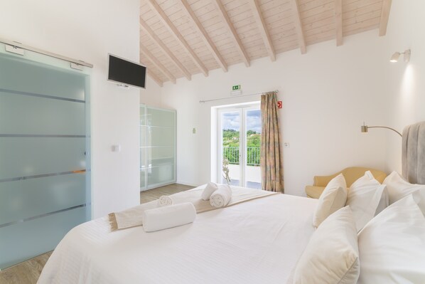 Ein Hotelzimmer mit Bett, Fernseher, einer Schiebetür und einem Balkon mit Blick.