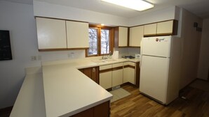 Una cocina con armarios de madera, encimera blanca, pileta integrada, refrigerador y ventana.