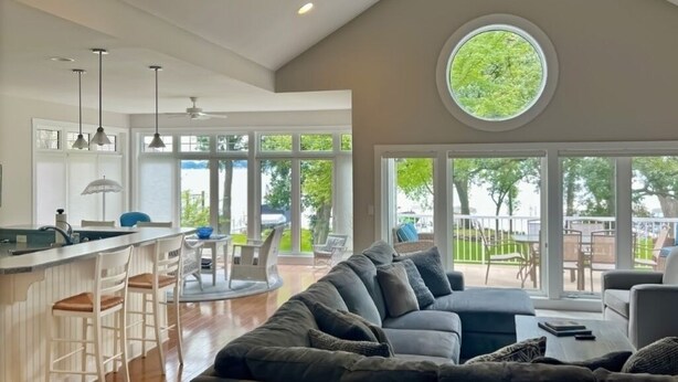 Un espacio habitable amplio con un sofá gris grande, una cocina con barra y grandes ventanales que ofrecen vistas al exterior.