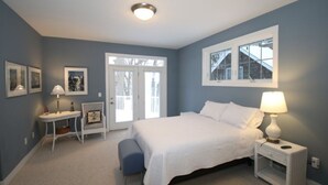 Un dormitorio con cama, mesita de noche, lámpara, silla y ventana.