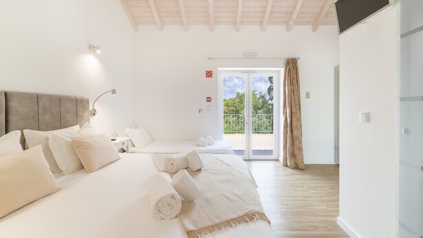 A hotel room with a large bed, a second smaller bed, a ceiling fan, a TV, and a sliding glass door to the outside. - Room 'Monte Do Sol 2' with Mountain View, Wi-Fi and Air Conditioning (S. Luís)