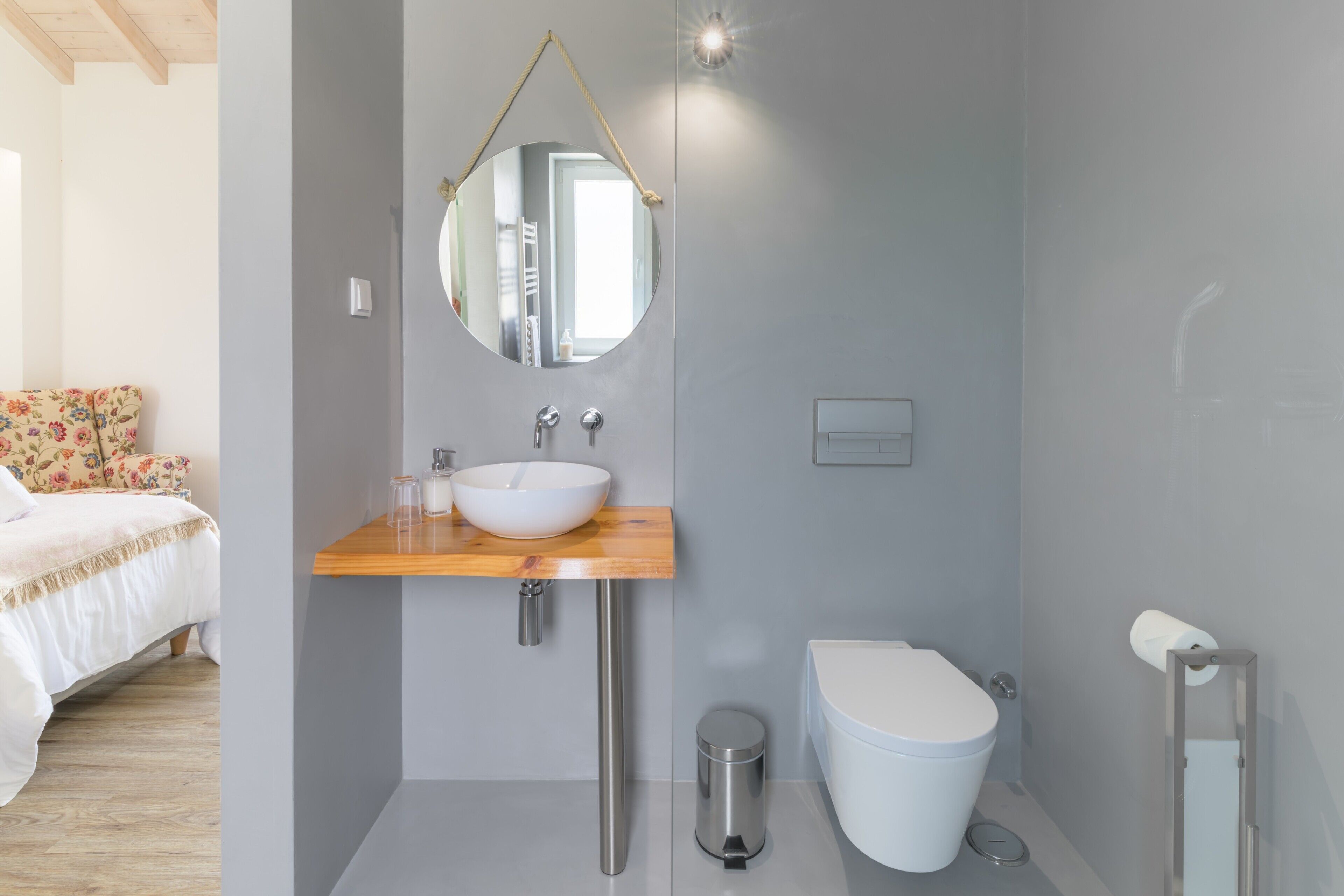 Une salle de bain moderne avec un meuble-lavabo en bois, un miroir rond, un lavabo blanc, des toilettes et une poubelle.