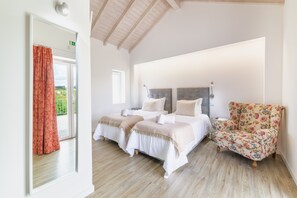 Une chambre avec deux lits, un fauteuil à motifs floraux et un grand miroir.