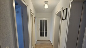 Käytävä, jossa on puulattia, valkoiset seinät ja ovi käytävän päässä.