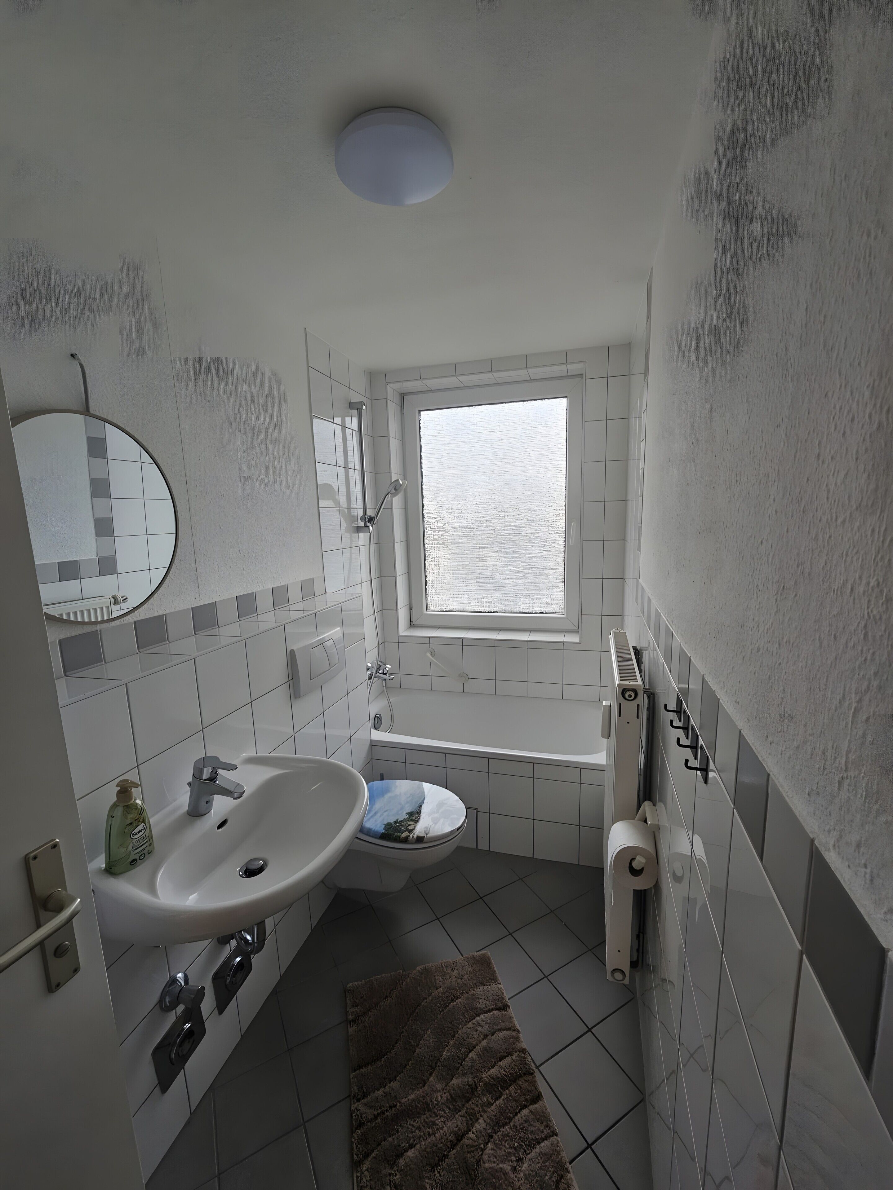 Een badkamer met een wastafel, toilet en ligbad, een raam en een spiegel.