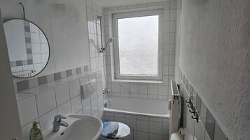 Een badkamer met een wastafel, toilet en ligbad, een raam en een spiegel.
