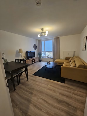 Een moderne woonkamer met een eettafel, bank, televisie en een groot raam.