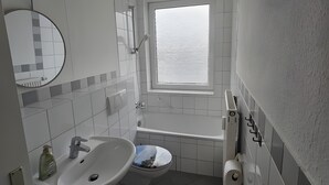 Kylpyhuone, jossa on pesuallas, wc, kylpyamme ja ikkuna.