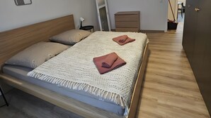 Moderni makuuhuone, jossa on puinen sänky, valkoinen, kuvioitu peitto ja riippuvalaisin.