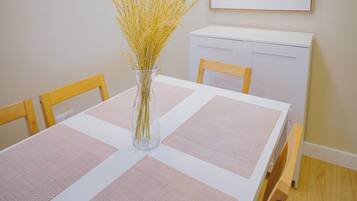 Un área de comedor con una mesa, sillas, un florero con plantas secas y una pizarra en la pared.