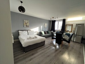 Une chambre d’hôtel moderne équipée d’un lit, d’un canapé, d’une table à manger avec des chaises, d’un réfrigérateur et d’œuvres d’art accrochées aux murs.