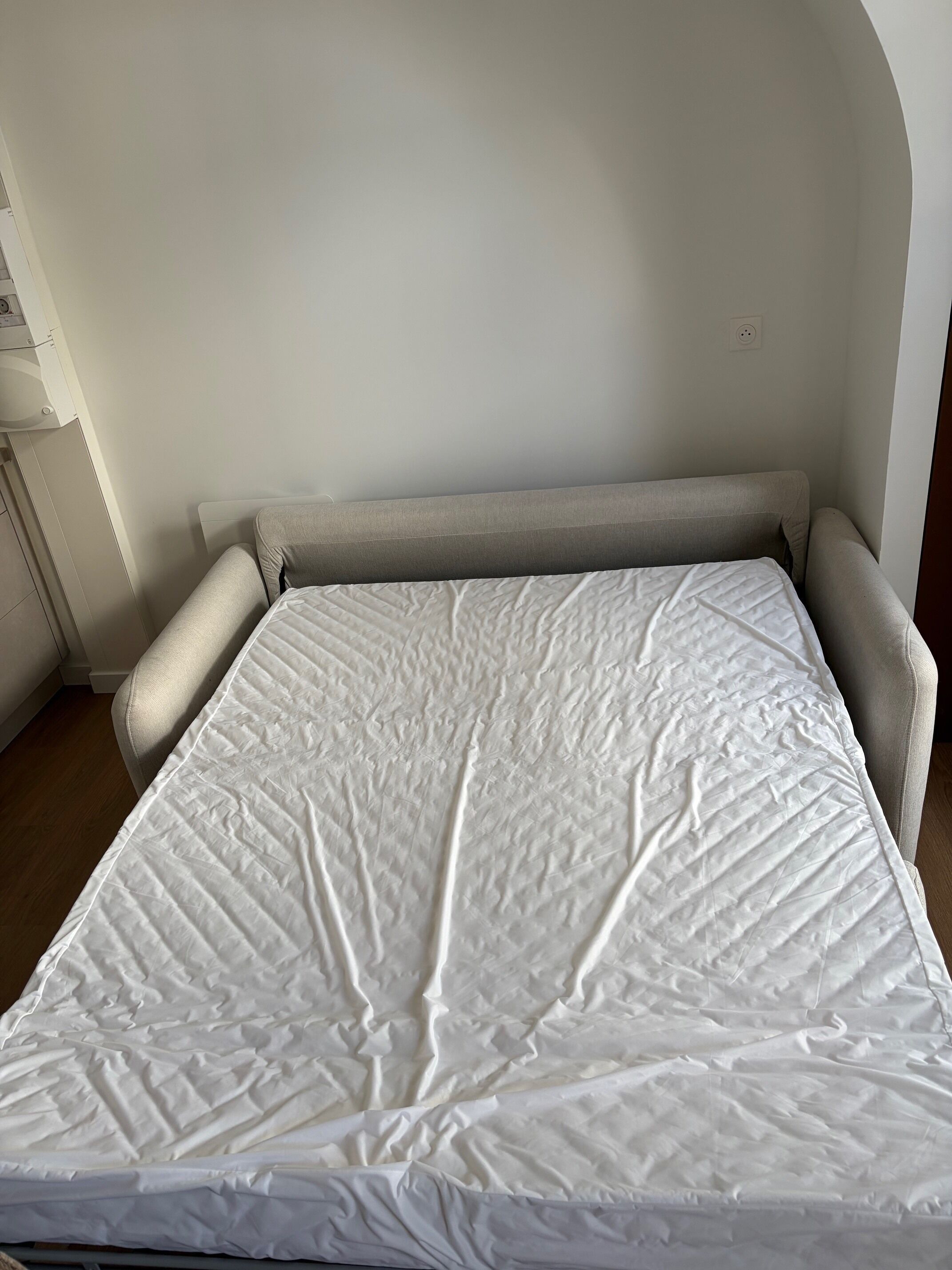 Un lit avec un matelas blanc et une tête de lit beige, dans une pièce aux murs blancs.