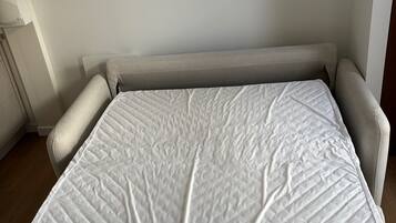 Un lit avec un matelas blanc et une tête de lit beige, dans une pièce aux murs blancs.