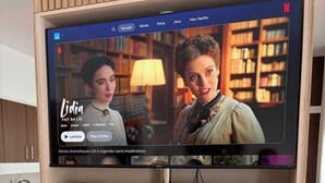 Uma televisão fixada numa parede de madeira, exibindo a interface da Netflix com um programa chamado 'Lidia'.