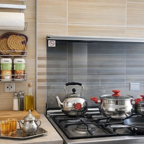 A kitchen with a gas stove, a kettle, a pot, and a tray with cups and a teapot. There are spice containers and a woven basket on the wall.