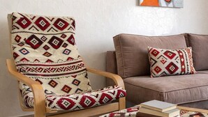 Una stanza con una poltrona a dondolo in legno, un tappeto decorato, un divano con un cuscino abbinato e un quadro appeso al muro.