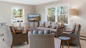 A living room with wicker furniture, a television, and large windows. - Drift Cottage Steps to Beach (Old Orchard Beach)