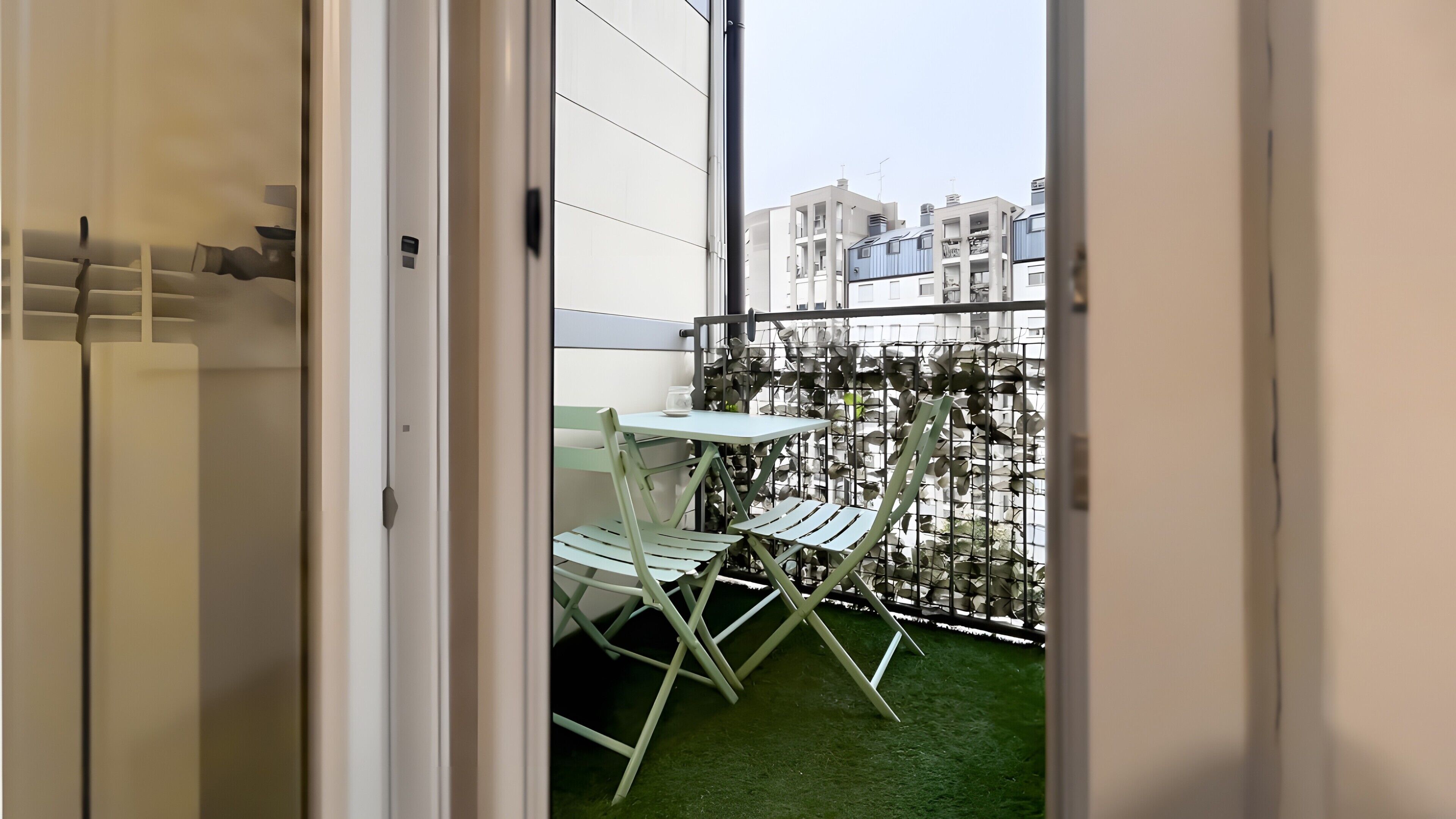 Un balcon avec un support à plantes en métal, une table et deux chaises.