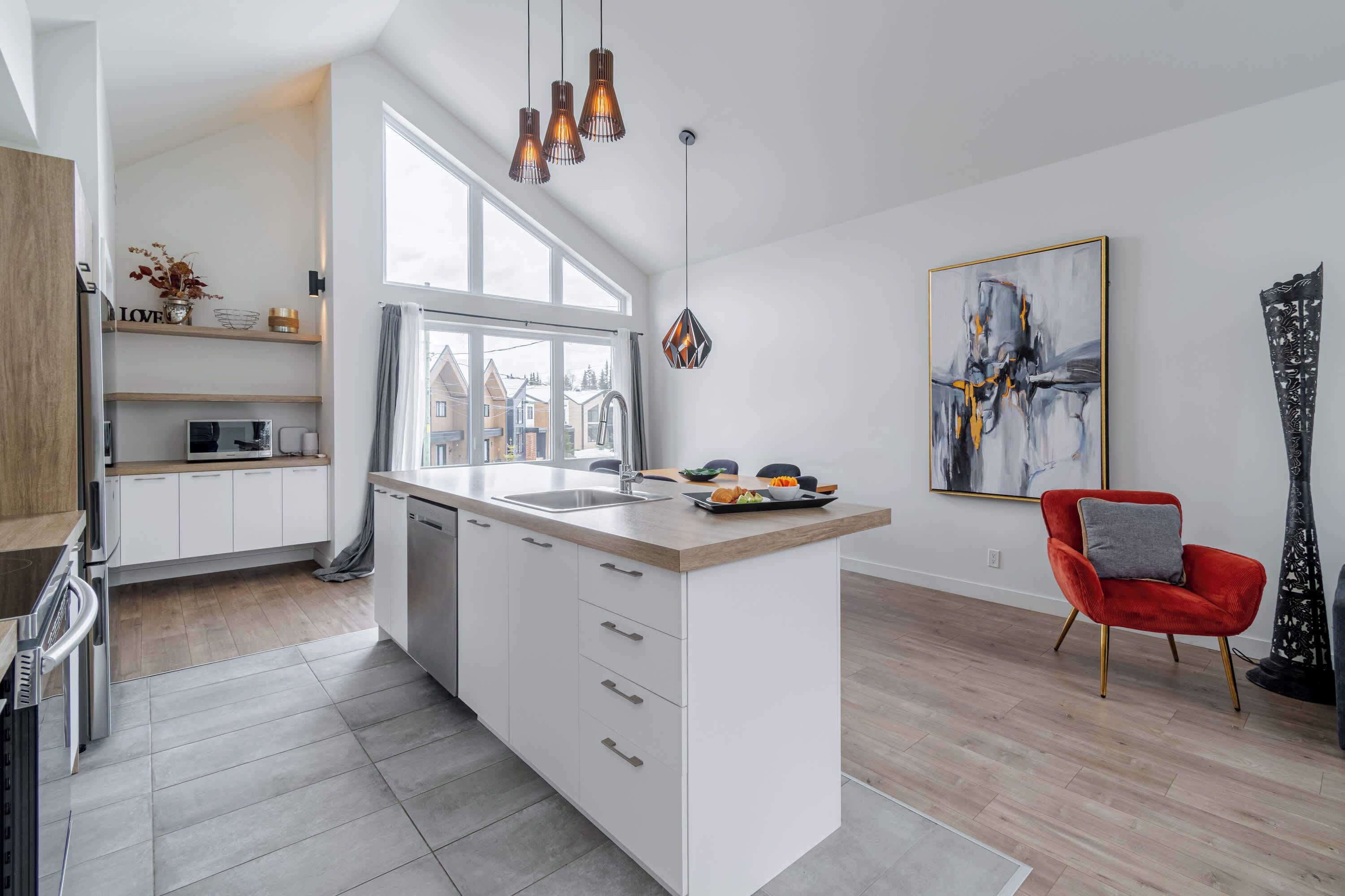 Una cocina moderna con armarios blancos, un ventanal grande y una silla roja.