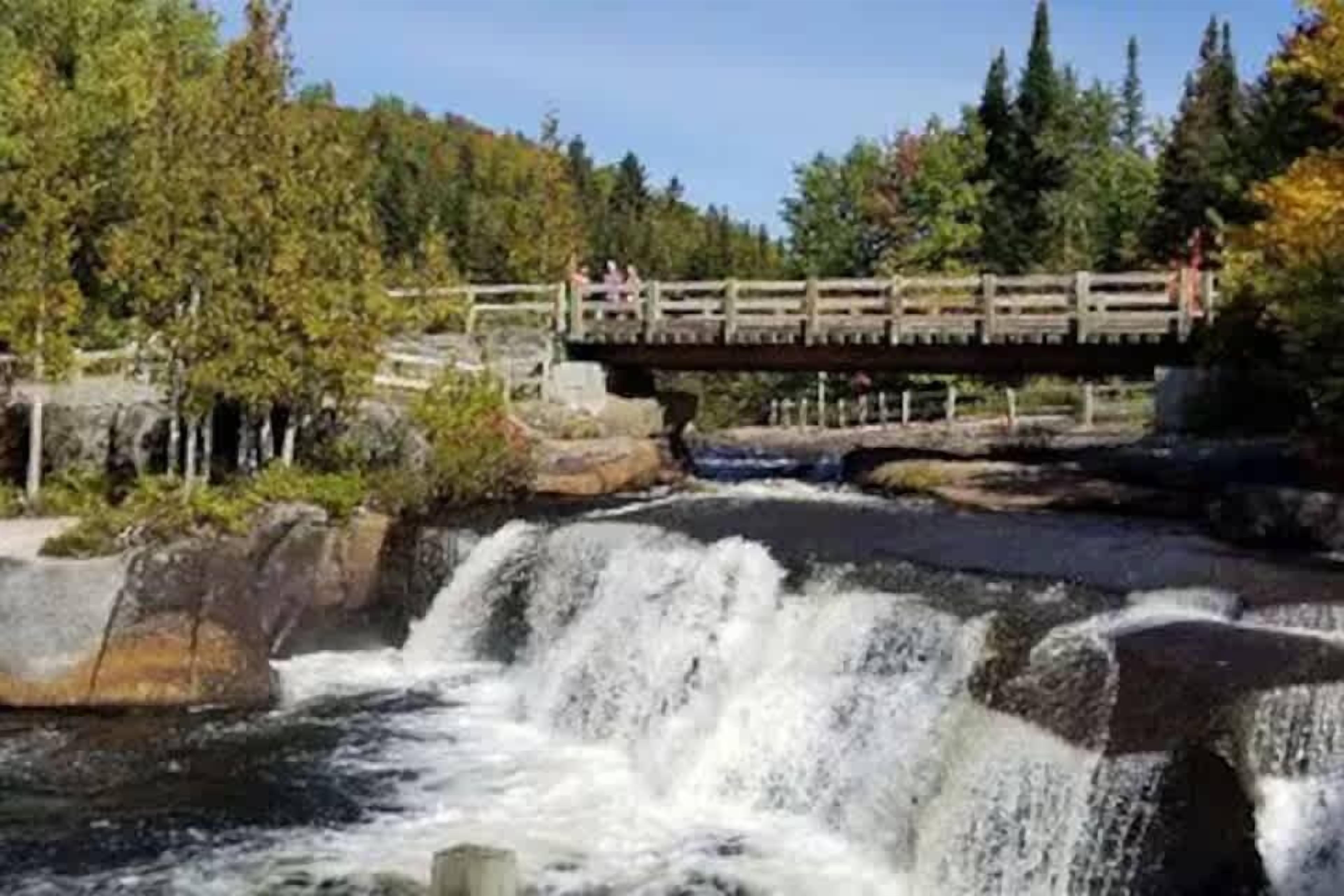 Eine Holzbrücke über einem Wasserfall, mit bewaldeter Kulisse.