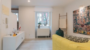 A room with a white radiator, a yellow sofa, a white cabinet, and a large abstract painting. - Apartment for rent at Rua de Santo Estevão 25, Santa Maria Maior, Lisbon. (Lisboa)