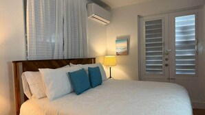Une chambre à coucher comprenant un lit, une table de chevet, une lampe, une fenêtre avec des rideaux et une porte avec des volets.