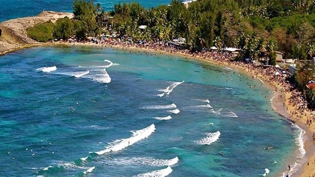 A beach with clear water, a crowd of people, and a line of trees. - Family Camper in Isabela (Isabela)