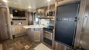 A compact RV kitchen with a microwave, stove, and refrigerator. - Family Camper in Isabela (Isabela)