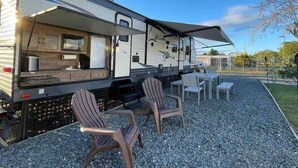 A recreational vehicle with a kitchen area, two chairs, and a table outside on a gravel surface. - Family Camper in Isabela (Isabela)