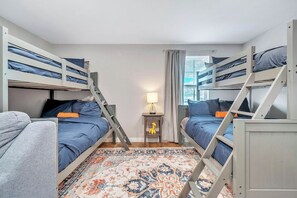 Ein Schlafsaalzimmer mit Etagenbetten, einem kleinen Tisch mit einer Lampe und einem gemusterten Teppich.