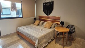 A bedroom with a bed, a small table, a chair, a hanging macrame wall decoration, and a window with a view. - Dream Studio Akua Tulum in Aldea Zama-Pool, Gym, Yoga, Coworking. (Tulum)