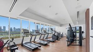 A gym with treadmills, elliptical machines, and weight equipment, large windows with a city view.