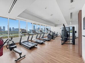 A gym with treadmills, elliptical machines, and weight equipment, large windows with a city view. - Luxe JVC Studio with Skyline Views, Pool and Gym (Dubai)